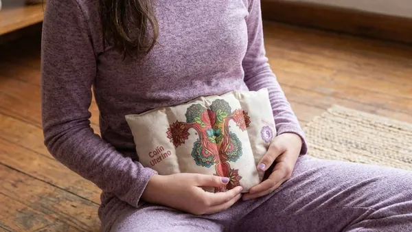 Mujer aliviando los cólicos menstruales con un cojín de semillas uterino
